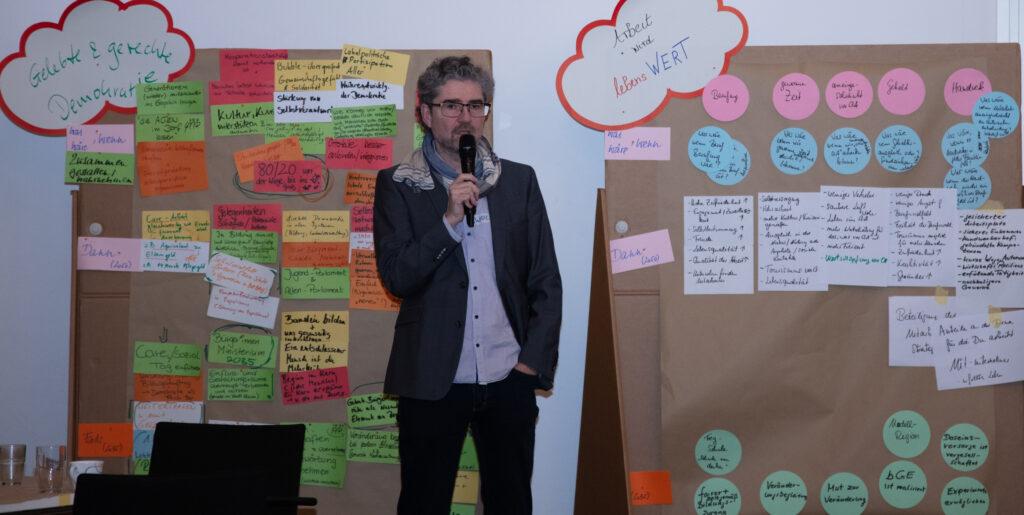 zwei Stellwände mit den Themen "Arbeit" und "Demokratie" stehen hinter  dem Organisator Wolf Hingst